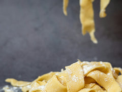 Świeży makaron pappardelle posypany mąką na ciemnym blacie