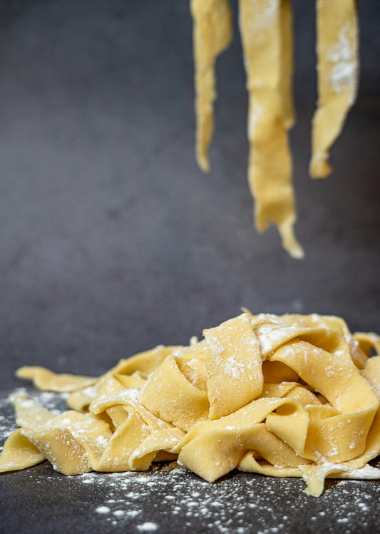 Świeży makaron pappardelle posypany mąką na ciemnym blacie