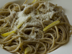 Spaghetti al limone ze startym serem i skórką z cytryny na białym talerzu