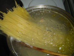 Spaghetti wkładane do garnka z wrzącą wodą i drewnianą łyżką