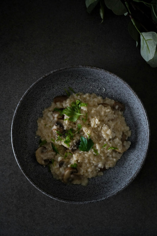 Risotto z grzybami posypane natką pietruszki w ciemnej misce