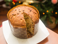 Pokrojone panettone z kroplami czekolady w papierowej formie, w tle świąteczna choinka