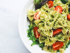 Sałatka makaronowa z farfalle, pesto i pomidorkami koktajlowymi na talerzu