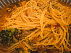 Spaghetti z brokułami posypane ziołami i serem na talerzu