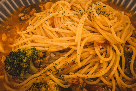 Spaghetti z brokułami posypane ziołami i serem na talerzu