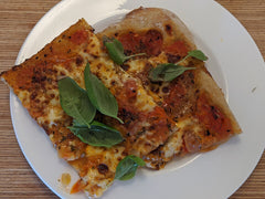 Pizza margherita na cienkim spodzie z listkami bazylii na białym talerzu